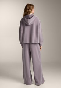 Tuta light lavanda con top cropped con cappuccio e pantaloni a gamba larga, realizzato in un tessuto morbido con una texture liscia.