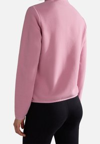 Roze fleecetrui met een gestructureerde afwerking, lange mouwen en een ronde halslijn. De zoom is netjes afgewerkt en wordt gedragen met zwarte leggings.