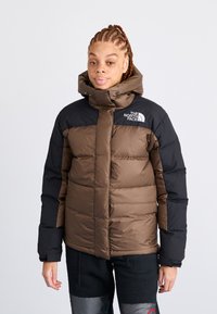 Smeđi i crni puf jakna s visokim ovratnikom, prednjim patentnim zatvaračem i logotipom The North Face na lijevom ramenu; sadrži kvadratne dijelove.