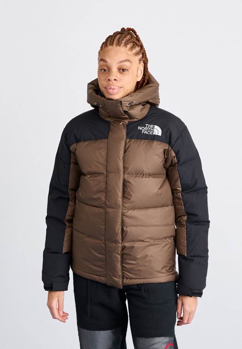 Smeđi i crni puf jakna s visokim ovratnikom, prednjim patentnim zatvaračem i logotipom The North Face na lijevom ramenu; sadrži kvadratne dijelove.