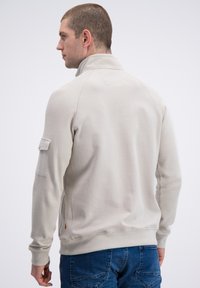 Lichtgrijze trui met gestructureerde schouderpanelen en een hoge kraag. Voorzien van geribbelde manchetten en een zijzakdetail. Gemaakt van zachte stof.