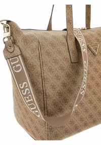 Sac à main en tissu à motif marron, comportant une fermeture éclair, deux poignées et une bandoulière amovible avec le mot "GUESS" en lettres blanches.