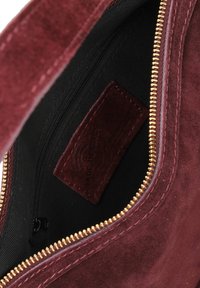 Interno della borsa in suede bordeaux con fodera nera, zip dorata e etichetta in pelle con la scritta "MADE IN ITALY". Inclusa tasca con zip.