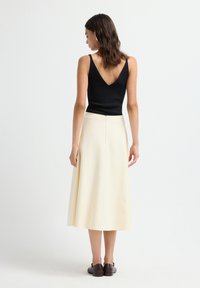 Zwarte V-hals tanktop gecombineerd met een crèmekleurige A-lijn midi rok, met een zijrits en een soepele, vloeiende textuur. Bruine schoenen maken de look compleet.