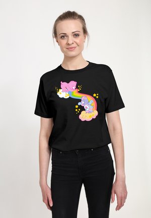 Femme portant un t-shirt noir avec un motif coloré de deux ours espiègles sur des nuages reliés par un arc-en-ciel avec des étoiles jaunes.