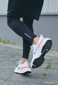 Scarpe da corsa Nike con tomaia in mesh bianco e dettagli viola, suola nera testurizzata e supporto per il tallone di un vivace arancione.