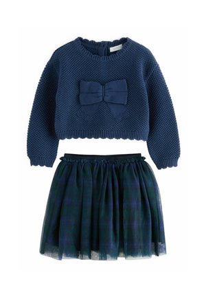 Granatowy sweter dzianinowy z detalem w postaci kokardy i okrągłym dekoltem, zestawiony z plisowaną spódnicą z tiulu w ciemnozielonym i niebieskim odcieniu.