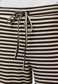 Pantalons lounge rayés avec des couleurs alternées marron et crème, une texture douce, une taille avec cordon de serrage ajustable et des poches sur les côtés.