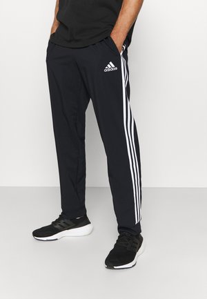 Czarne sportowe spodnie z białym, trzy-paskowym wzorem po bokach, wykonane z lekkiego materiału, zestawione z czarnymi trampkami.