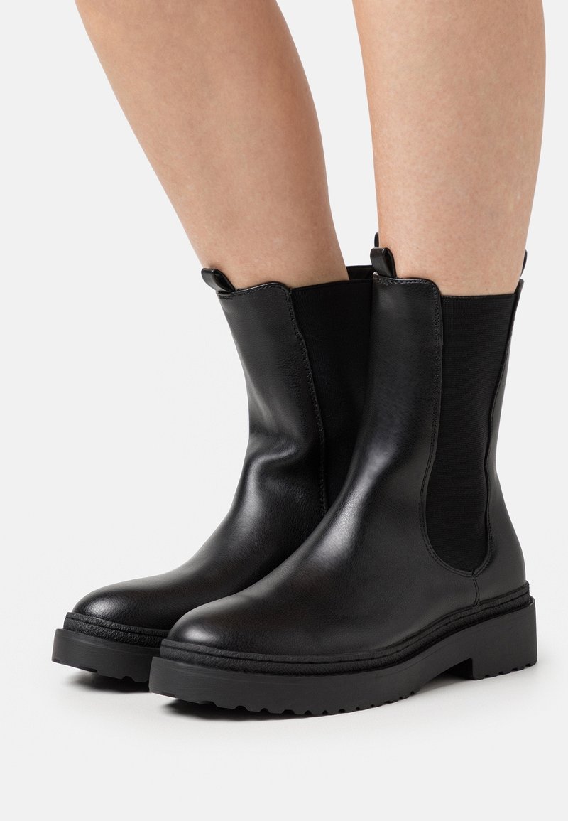 Botines de cuero negro con paneles laterales elásticos, lengüetas para tirar y suela de goma texturizada. Acabado liso y diseño de puntera redondeada.