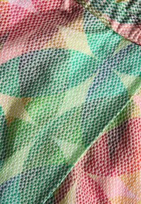 Tissu coloré avec une texture en maille présentant un motif géométrique dans des tons de vert, rose et jaune. Structure diagonale notable visible.