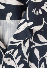 Camisa navy con un print botánico blanco, con cierre de botones y una tela texturizada. El cuello presenta un diseño clásico con bordes curvados.