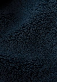 Mørk marineblå, blødt stof med en tekstureret, luftig overflade. Materialet viser tætte, ujævne løkker, der skaber et blødt og taktilt udseende.