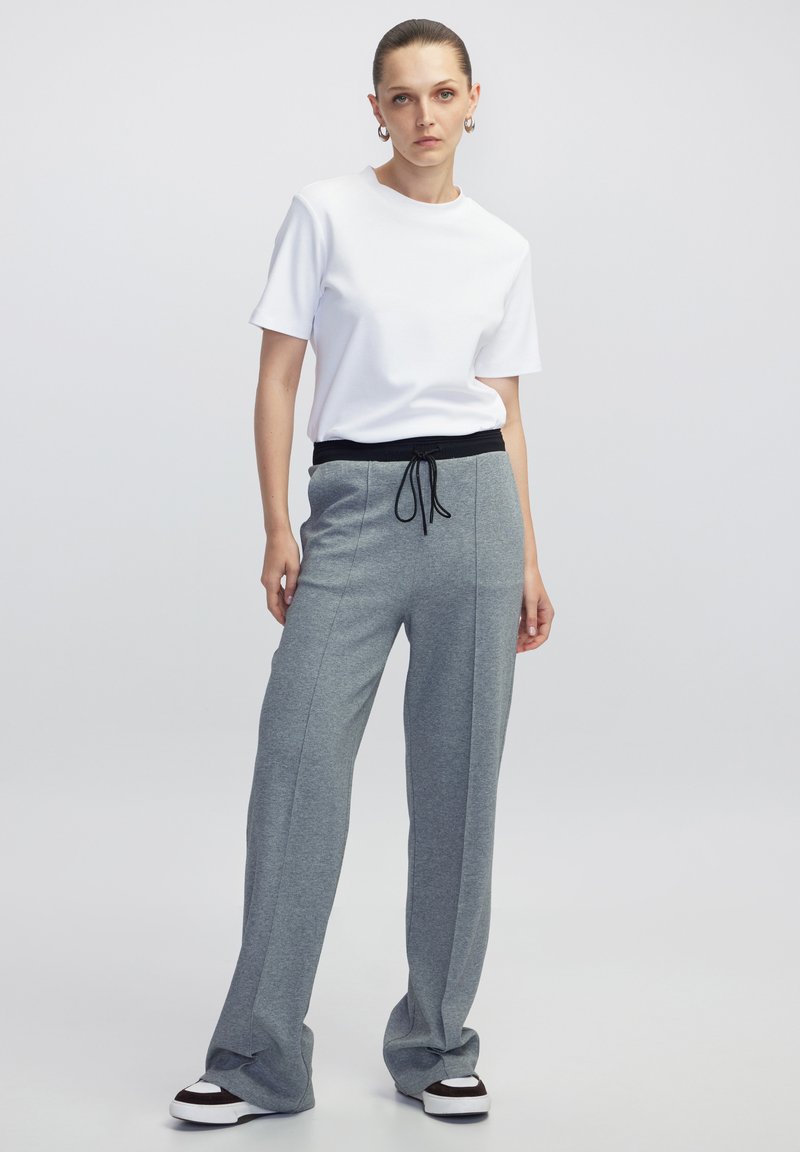 T-shirt bianco a maniche corte abbinato a pantaloni della tuta grigi a gamba larga con vita regolabile nera e scarpe da ginnastica bianche.