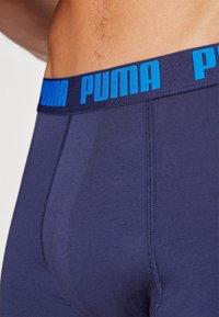Tamno plave bokserice od glatkog materijala, s širokim elastičnim pojasom na kojem je istaknuta plava oznaka "PUMA".