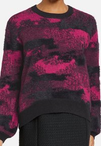 Suéter de punto difuso con un atrevido patrón abstracto en rosa y negro, cuello acanalado y un ajuste ligeramente oversize con un dobladillo negro.