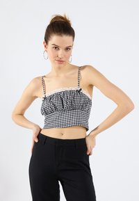 Sort og hvid ternet cropped top med flæser af blonder og justerbare stropper, parret med højtaljede sorte bukser.