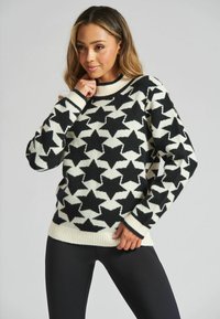 Maglione a righe bianche e nere con motivo a stelle, caratterizzato da un collo e polsini a costine, un fit morbido e una texture soffice. Abbinato a leggings neri.