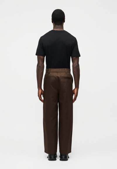 Black t-shirt with short sleeves, paired with brown wide-leg pants featuring back pockets and an elastic waistband. Black shoes complete the outfit.