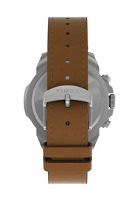Timex laikrodis su rusvu odiniu dirželiu, nerūdijančio plieno sagtimi ir pilka korpusu. Pasižymi matomais siuvinėjimais ir keliais reguliavimo skylėmis.