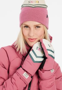 Roze geïsoleerde jas, lichtroze gebreide muts en witte handschoenen met chevronpatronen in groen en roze. Labels zichtbaar op de mouwen en handschoenen.