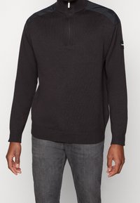 Pullover grigio scuro con colletto a mezza zip, polsini e orlo a costine, e pannelli in nylon nero sulle spalle. Tessuto a maglia testurizzato.