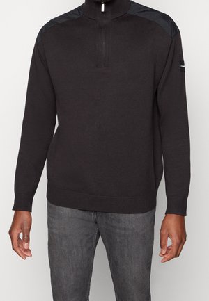 Sweat-shirt à col zippé demi avec un gris foncé, des poignets et un ourlet côtelés, et des panneaux en nylon noir sur les épaules. Tissu en tricot texturé.
