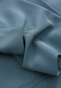 Modro teksturirano blago, ki se ohlapno zloži, z mehkimi gubami in gladko površino z rahlo rebrastostjo ter čistim zaključkom.