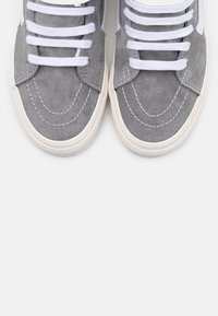 Szare zamszowe trampki z białymi sznurowadłami i kontrastującymi przeszyciami. Zaokrąglony nosek i teksturowana gumowa podeszwa zapewniająca przyczepność. Prosty, klasyczny design.