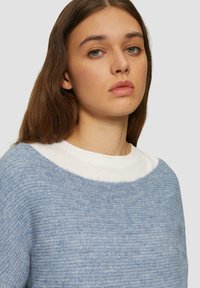 Lichtblauwe trui met een gestructureerd breipatroon, ruime halslijn en een onderliggende witte shirt. Zacht materiaal en een casual pasvorm.
