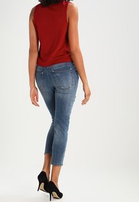 Červený top bez rukávů v kombinaci s modrými džínami s mírným vzestupem a černými vysokými podpatky, vybavený náprsními kapsami a přiléhavým střihem.