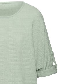 Helles, strukturiertes Oberteil in Grün mit Rundhalsausschnitt, hochgekrempelten Ärmeln, die mit Knöpfen gesichert sind, und einem leicht lockeren Schnitt.