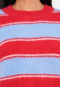 Maglione lavorato a maglia con strisce orizzontali in rosso brillante, azzurro chiaro e bianco. Texture morbida e pelosa con scollatura a coste.