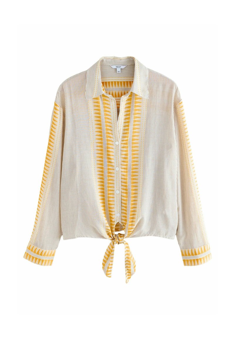 Chemise beige à manches longues avec fines rayures et motifs triangulaires jaunes verticaux, boutonnée sur le devant et nouée à la taille.