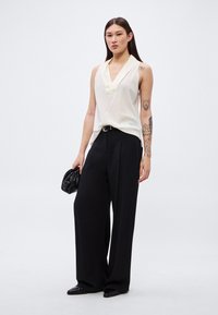 Ελεφαντόδοντο αμάνικη μπλούζα με λαιμόκοψη σε σχήμα V, συνδυασμένη με μαύρο παντελόνι φαρδύ με ψηλή μέση. Μαύρο τσαντάκι φάκελος και μυτερά φλατ παπούτσια ολοκληρώνουν το ντύσιμο.