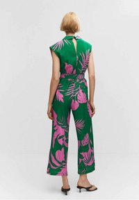 Combinaison verte avec des motifs de feuilles roses, manches courtes, taille ceinturée et design dos nu ; silhouette à jambes larges et texture lisse.