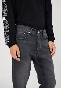 Maglietta nera a maniche lunghe con stampe grafiche bianche; jeans grigi con cinque tasche, borchie in metallo, vestibilità dritta e una texture scolorita.