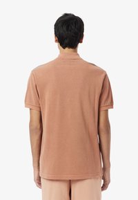 Kortärmad, blek rosa polo med krage, mjuk textur och avslappnad passform. Ingen synlig logotyp eller mönster.