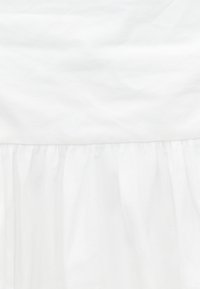 Tissu blanc avec une couture et un volant froncé en bas, montrant la texture et des plis doux.