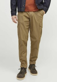 Khaki cargo broek met zijzakken, een relaxte pasvorm en lichte stof. Draagt een bruine t-shirt en een donkerblauwe denim jacket.