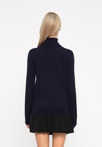 Navy turtleneck sweater made of smooth knit material, long sleeves, fitted silhouette, paired with a black pleated skirt.