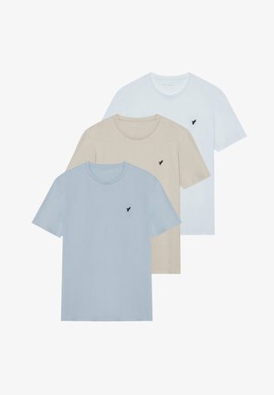 Trzy koszulki z krótkim rękawem ułożone jedna na drugiej: jedna blado niebieska, jedna beżowa, jedna biała. Każda ma okrągły dekolt i małe czarne logo na piersi.