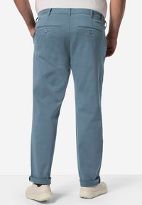 Ljusblå bomullbyxor med avslappnad passform, utrustade med två bakfickor med knappstängningar och uppvikt fåll, som bärs med vita sneakers.