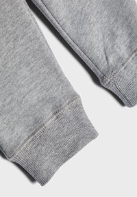 Pantalons de survêtement en coton gris présentant des poignets côtelés, une texture lisse et une coupe droite. Détails de couture visibles le long des coutures.