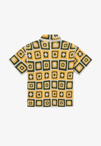 Chemise en tricot à manches courtes avec des motifs carrés au crochet en vert, jaune et blanc, vue de dos sur un fond blanc.