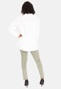 Hvid langærmet skjorte med knaplukning i tekstureret stof, parret med lysegrønne skinny jeans og sorte højhælede sko.