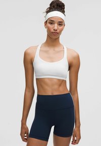Sujeción deportiva blanca y pantalones cortos azul marino, fabricados en una tela suave. El sujetador tiene tirantes anchos y un diseño limpio; los pantalones cortos cuentan con una cinturilla alta.