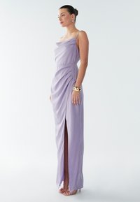 Lavendli värvi satiinist kleit, millel on drapeeritud kaelus, külgedel kortsud, reie kõrgune lõhik ja õhukesed rihmad, kantud läbipaistvate kontsadega.