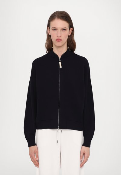 Schwarze Strickjacke mit Reißverschluss, hohem Kragen, lockeren Ärmeln, Fronttaschen und silbernen Reißverschlussdetails. Glatte Textur mit minimalistischer Gestaltung.