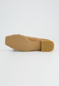 Chaussure en daim marron clair avec un bout arrondi, un talon bas et une semelle en caoutchouc. Présente un logo embossé et une texture lisse sur la tige.